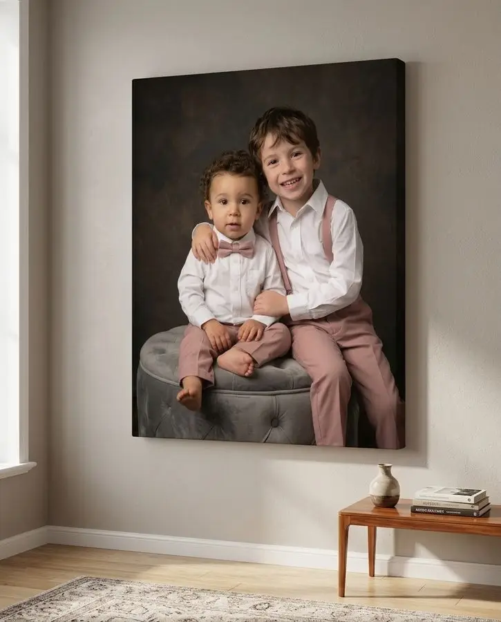 An older boy sits with his arm around his toddler brother, both wearing white dress shirts and dusty rose trousers against a dark backdrop.