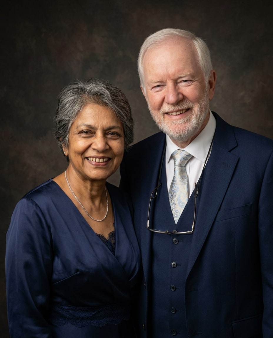 A smiling senior couple poses closely together wearing formal navy blue attire against a dark textured background.