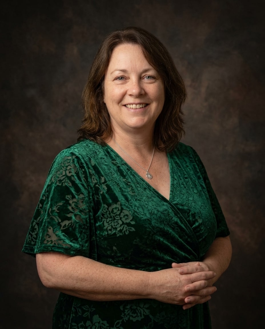 A smiling woman with shoulder-length brown hair poses in an emerald green velvet dress against a dark textured background.